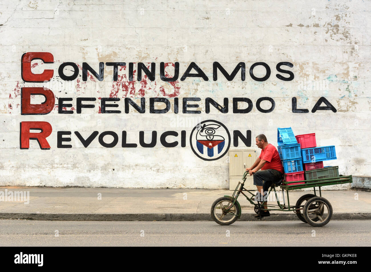 A Cuban man cycles past a revolutionary wall mural in Havana, Cuba Stock Photo