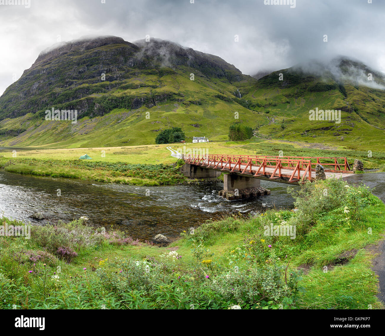 A bridge over the river Coe with Achnambeithach cottage nestled under the mountains Stock Photo