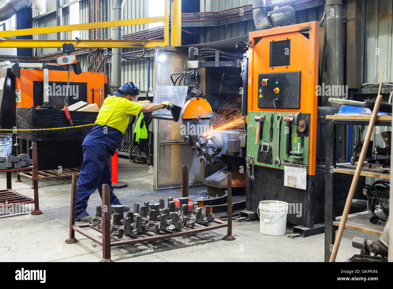 workman grinding and cutting away cast metal components from its 'casting' tree. Stock Photo