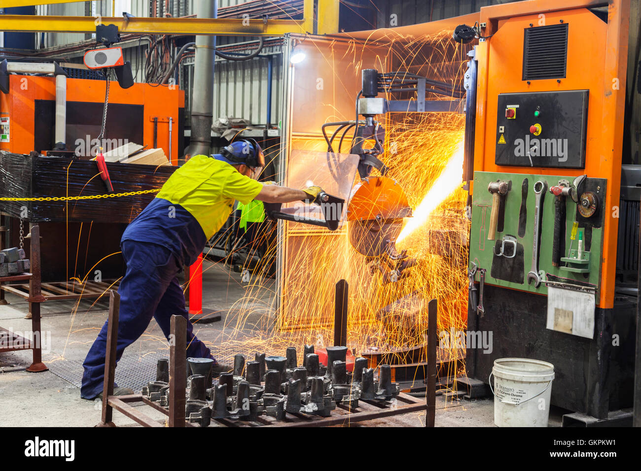 workman grinding and cutting away cast metal components from its 'casting' tree. Stock Photo