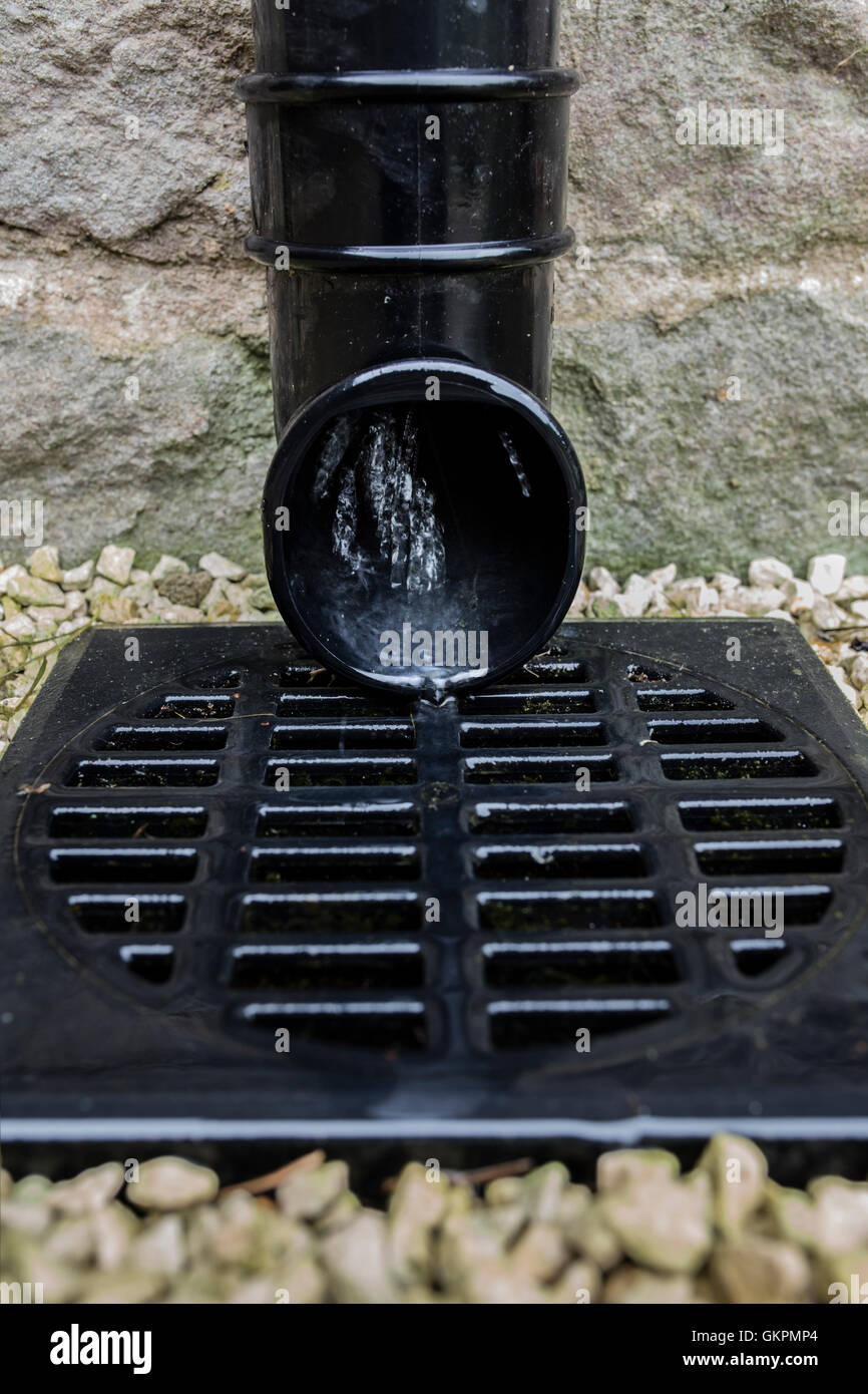 Water flowing from a gutter downpipe into a storm drain. Stock Photo