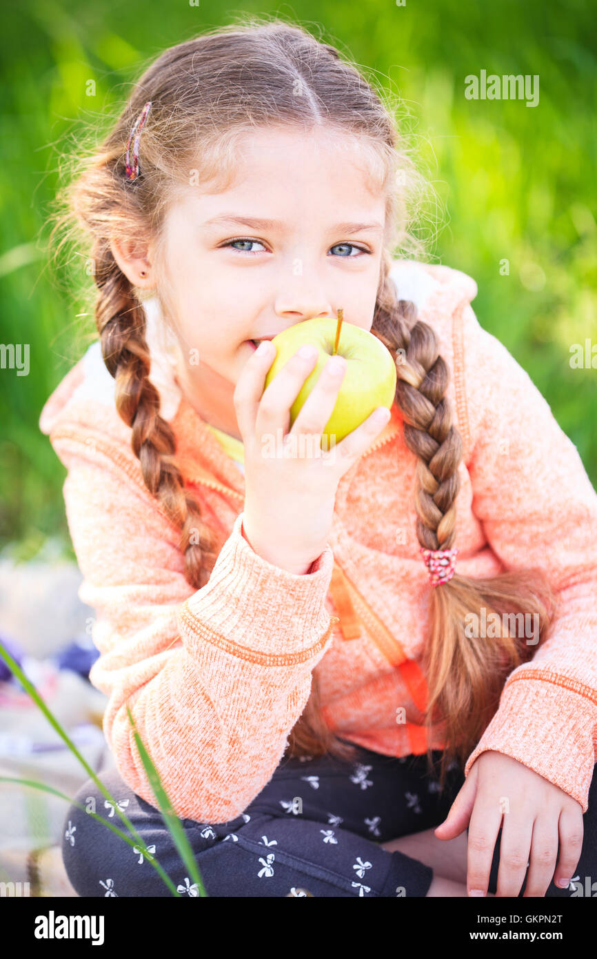Little cute girl in the garden on a background of green grass with an apple in her hand Stock Photo