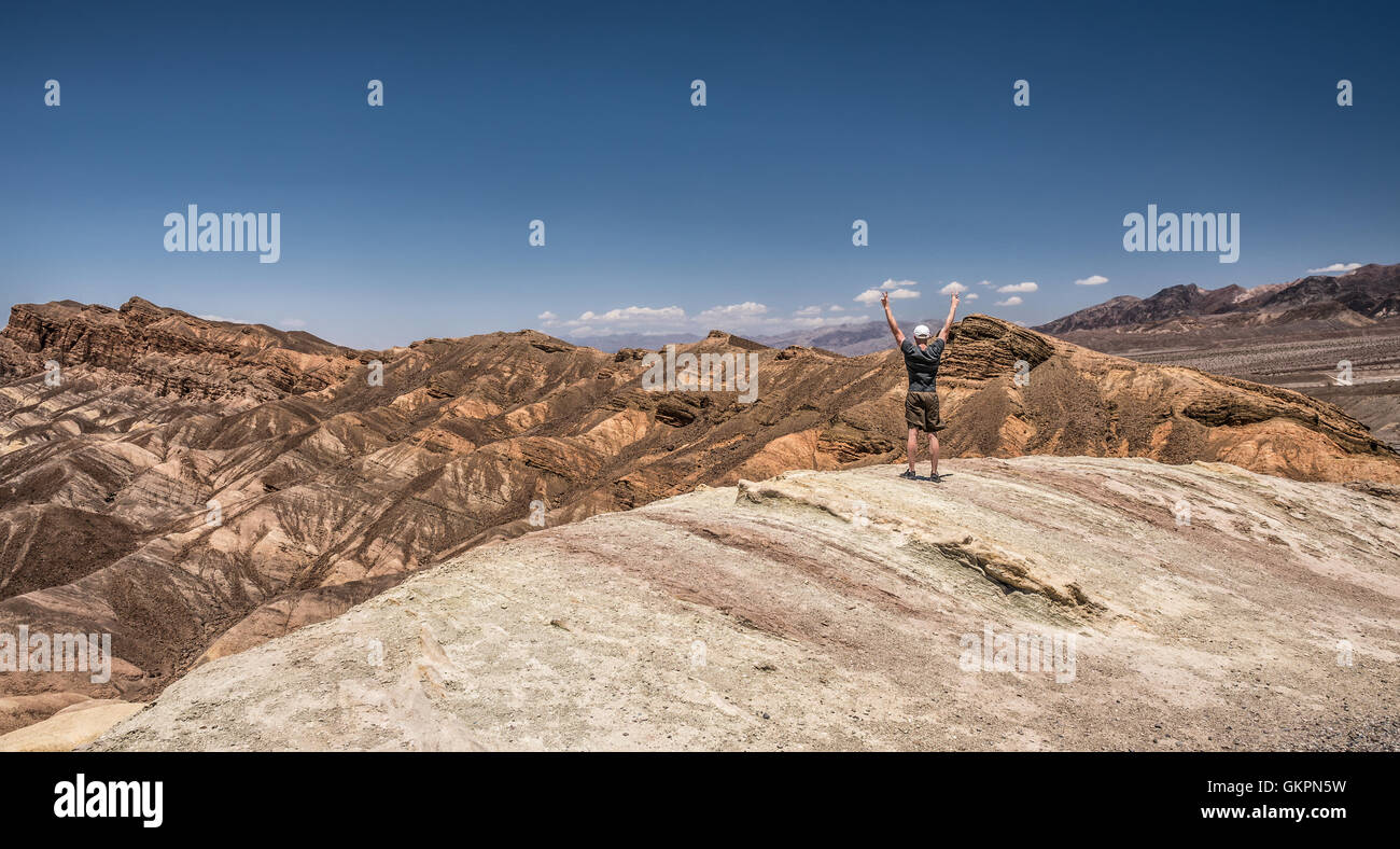 Death Valley and a happy hiker standing on the rim with arms raised up. Winner, success and achievement  concept in nature. Stock Photo