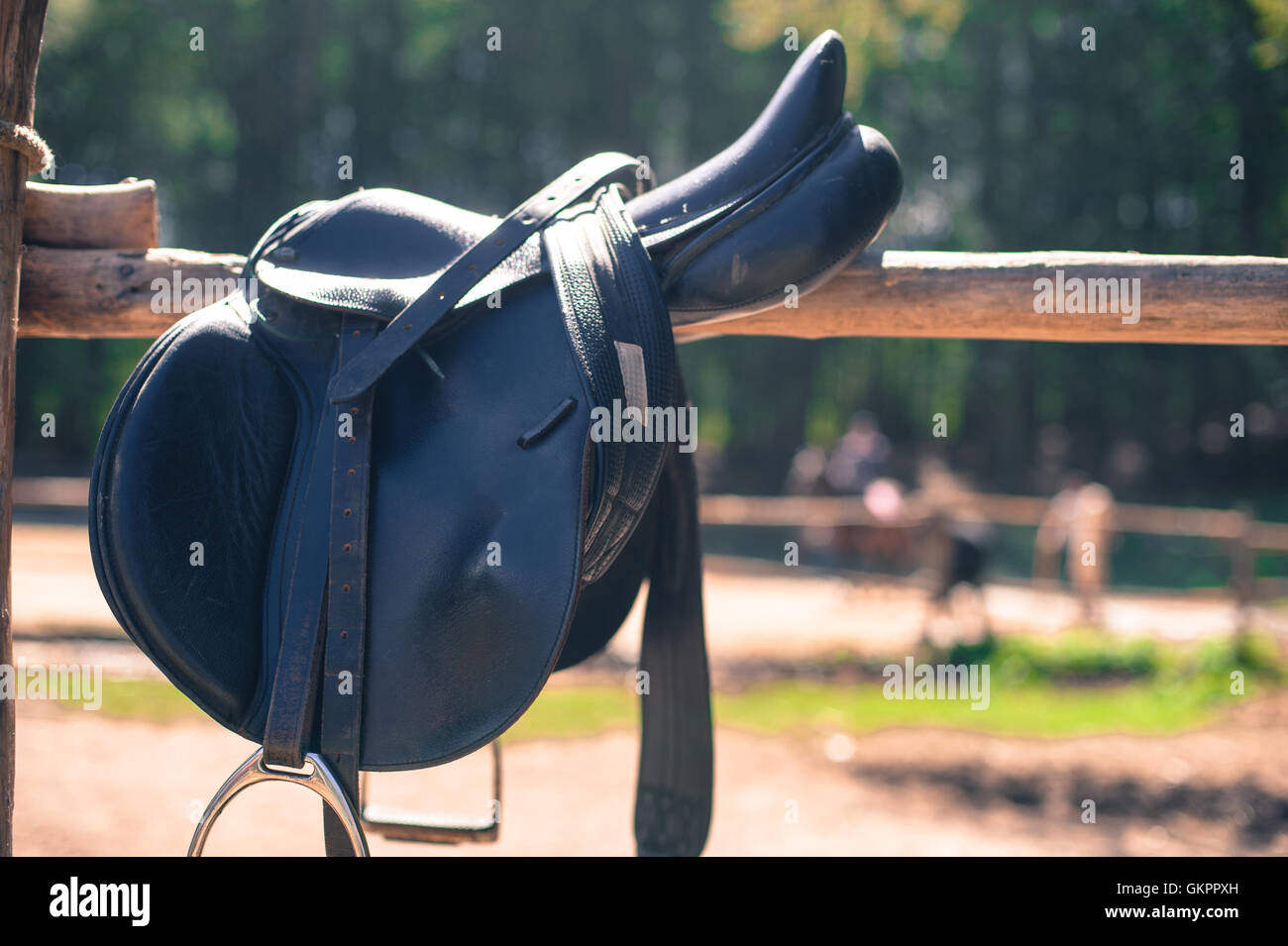 Horse saddle close up on stables fence out of focus background with people riding autumnal colors Stock Photo