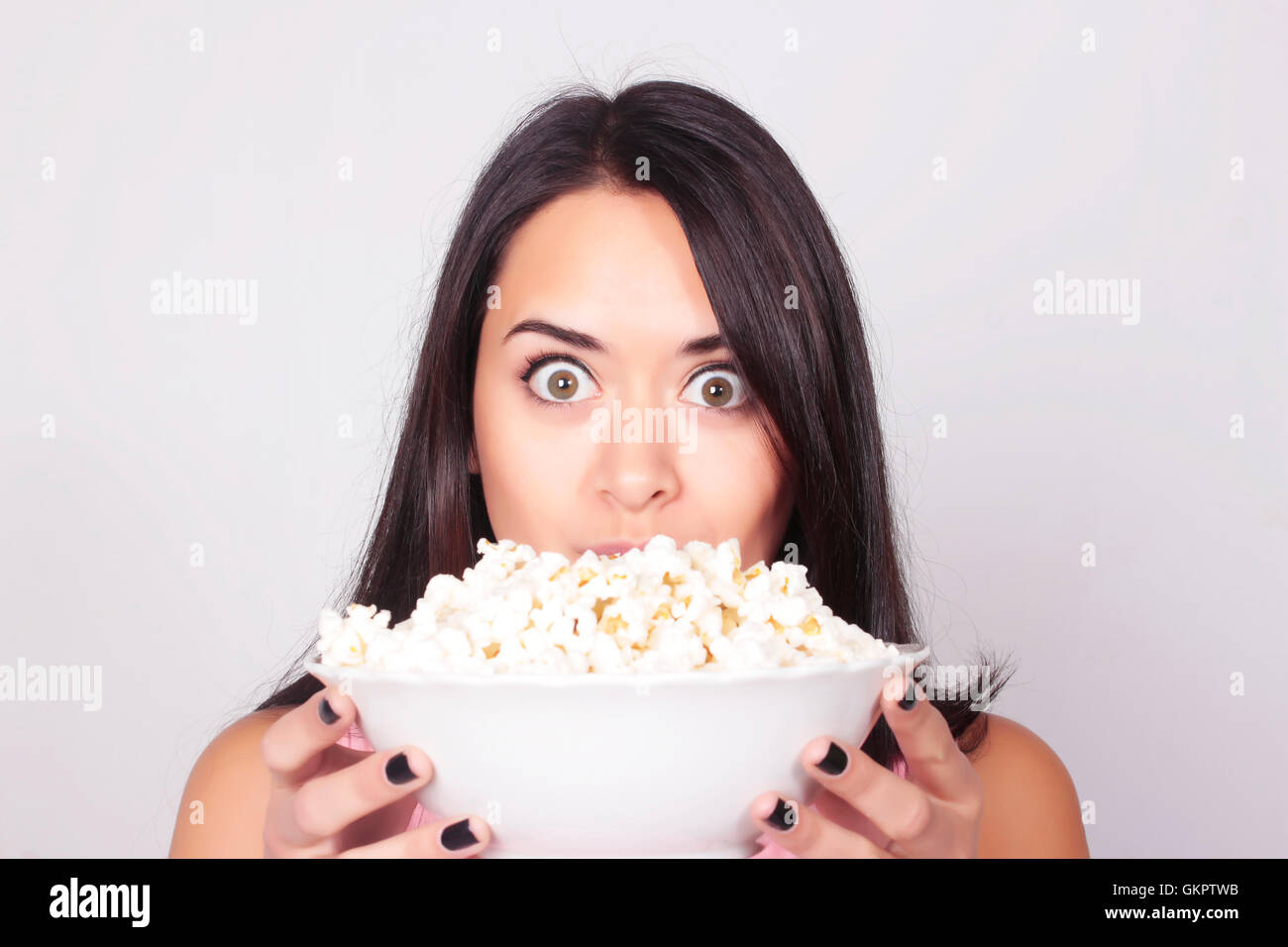 Young caucasian woman watching a movie / TV, while enjoying a snack. Girl eating popcorn. Leisure time. Stock Photo