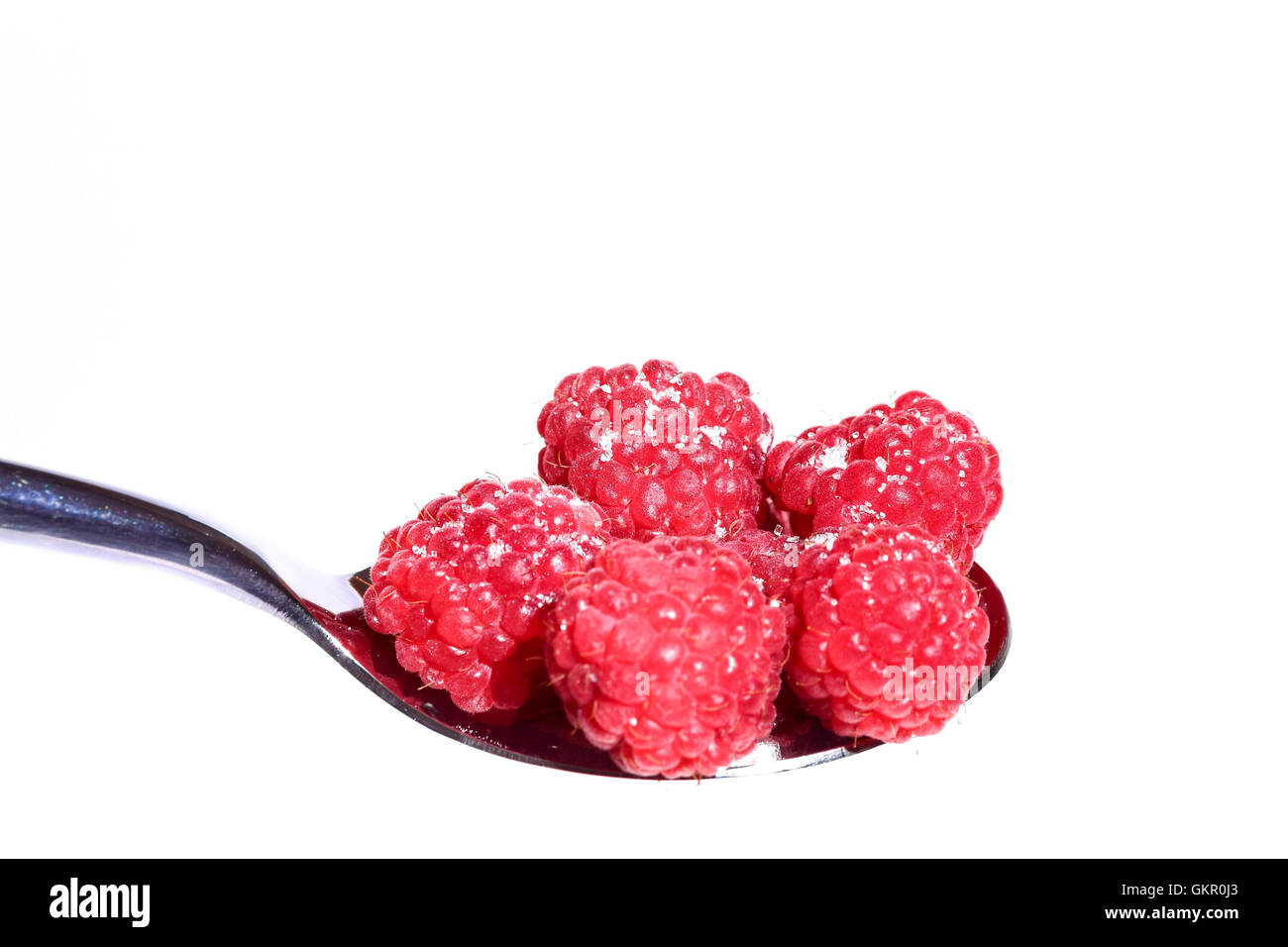 Ripe organic raspberries heaped on a metal dessert spoon studio shot