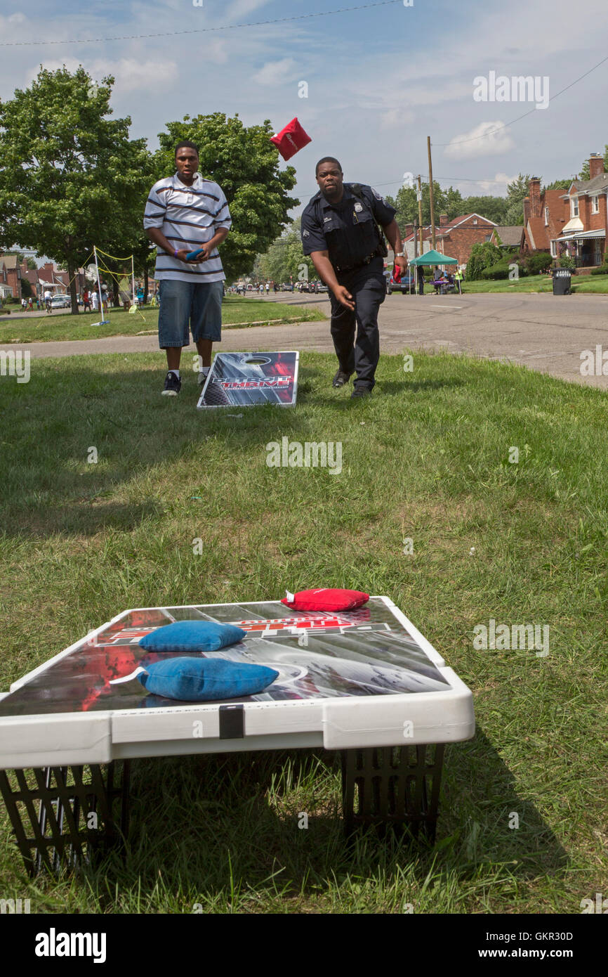 Detroit, Michigan - Neighborhood groups hold a summer street fair. A policeman joins community members in playing cornhole. Stock Photo