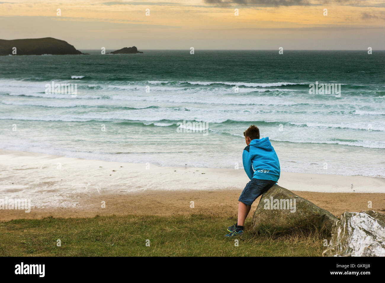 A young boy sits on a rockoverlooking Fistral in Newquay, Cornwall. Stock Photo