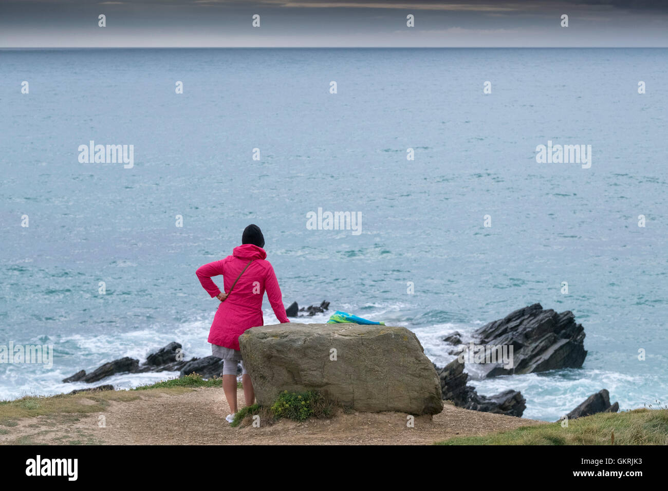A woman wearing a brightly coloured coat looking out to sea on The Headland in Newquay, Cornwall. Stock Photo