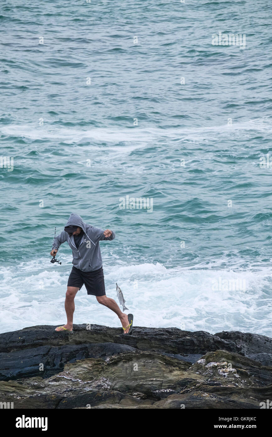 A holidaymaker fishing from rocks at Fistral in Newquay, Cornwall. Stock Photo