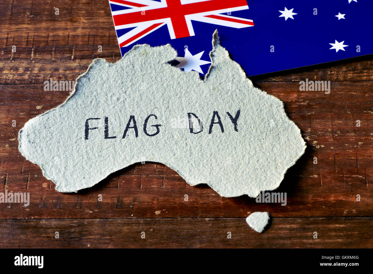 closeup of an Australian flag and a piece of paper cut in the shape of Australia with the text flag day handwritten in it Stock Photo