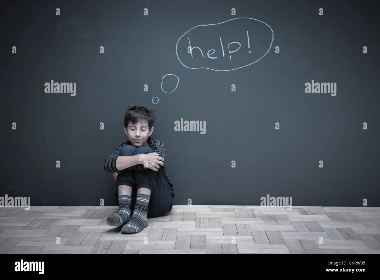 Boy sitting on floor hugging knees with 'help' written on wall Stock Photo