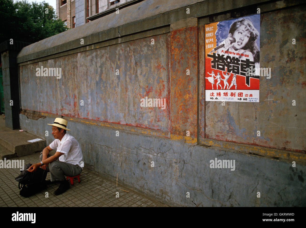 man crouching down next to wall with pop music poster, Shenyang, China. Stock Photo