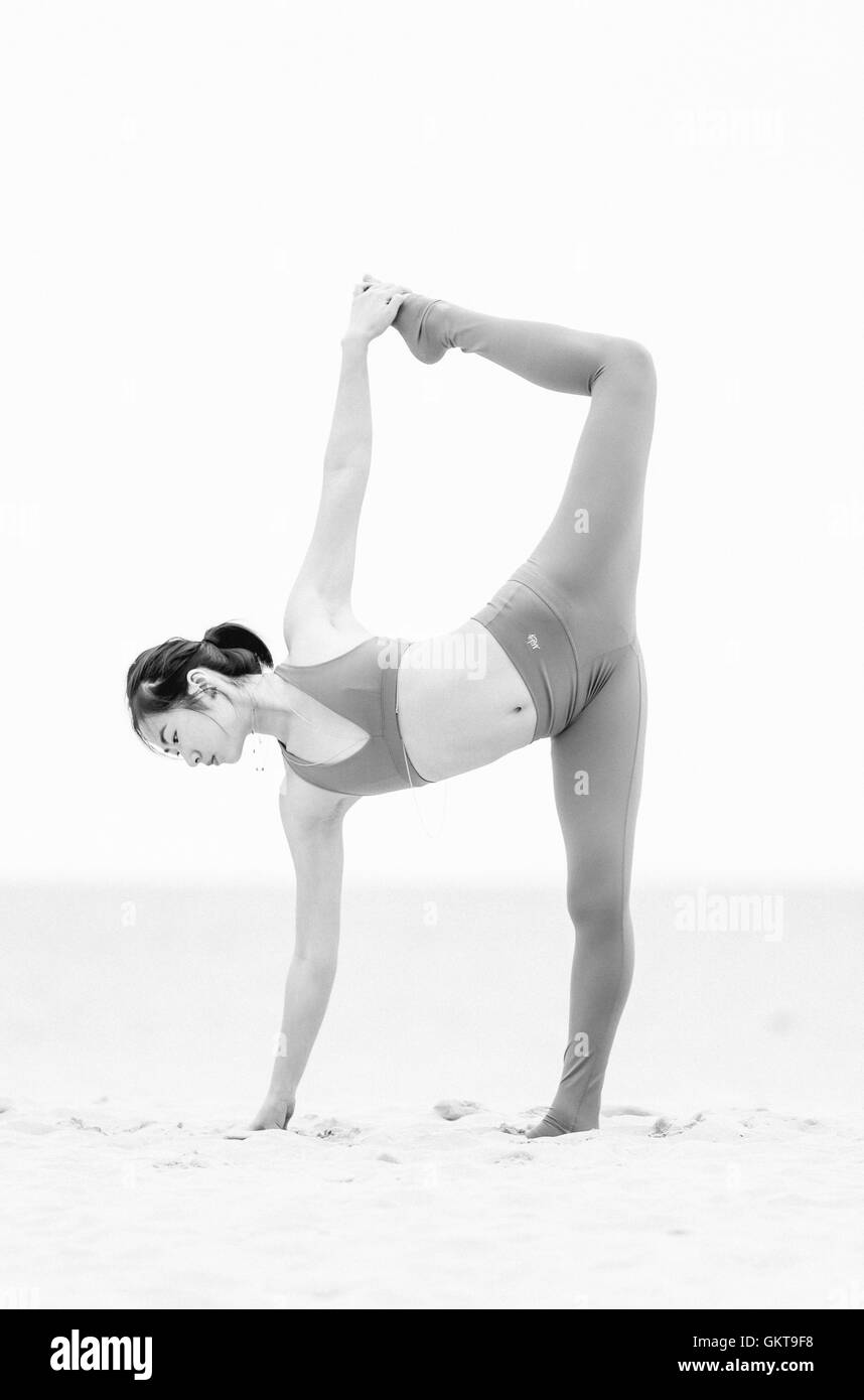 Chinese woman in orange doing yoga on the beach. Stock Photo