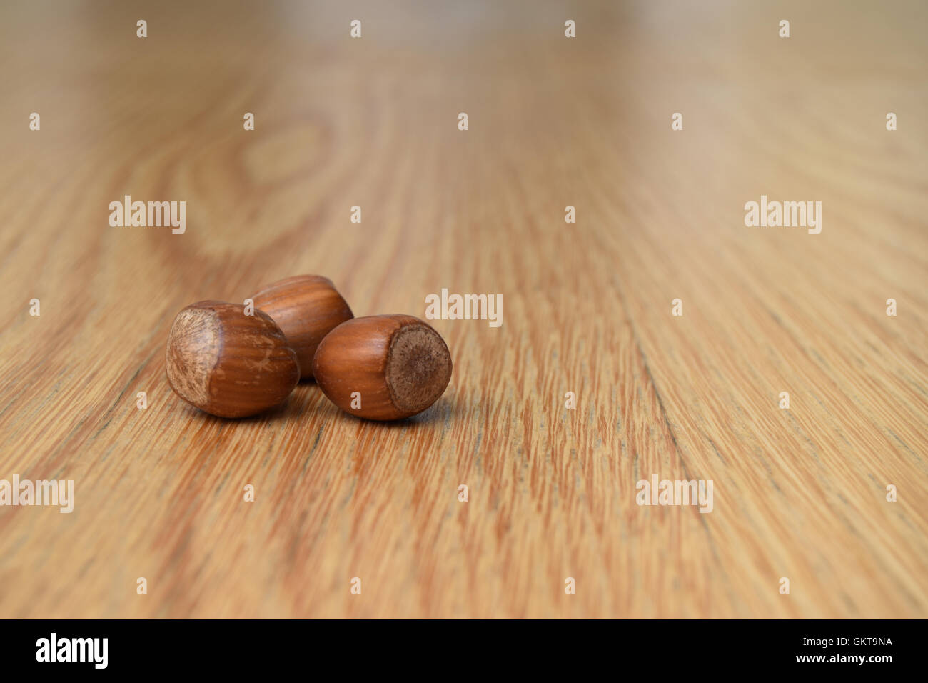 Three hazelnuts sitting together on a wooden table, close up Stock Photo