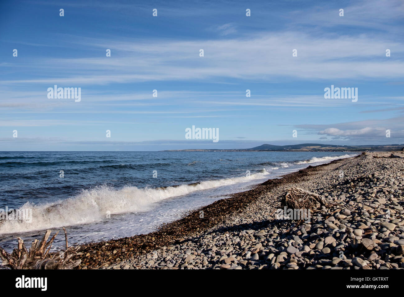 Waves crash on pebble beach on Scottish coastal village of Spey Bay with Moray Firth coastline in background Stock Photo