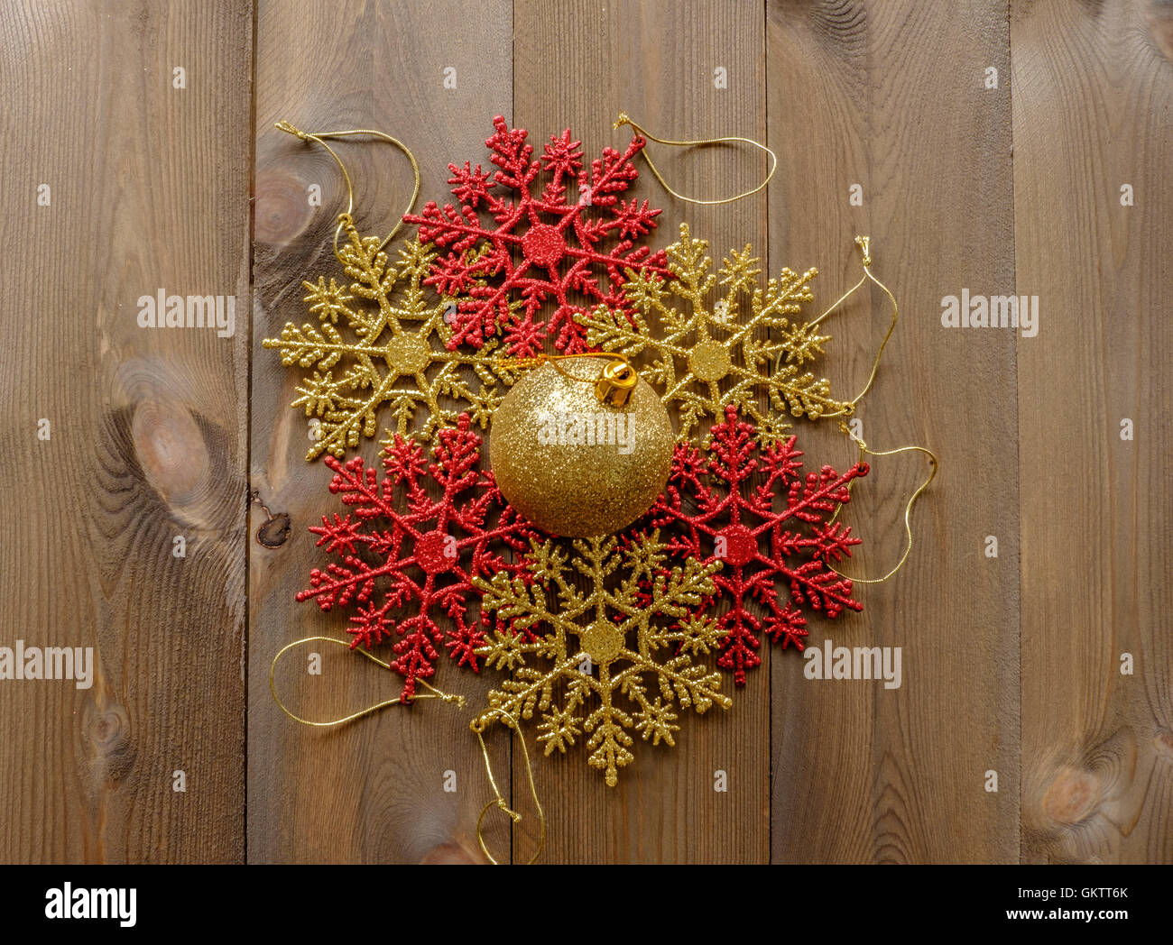 Group of sparkly Christmas tree decorations lay flat on wooden background. Red and gold glitter snowflakes in circle with one go Stock Photo