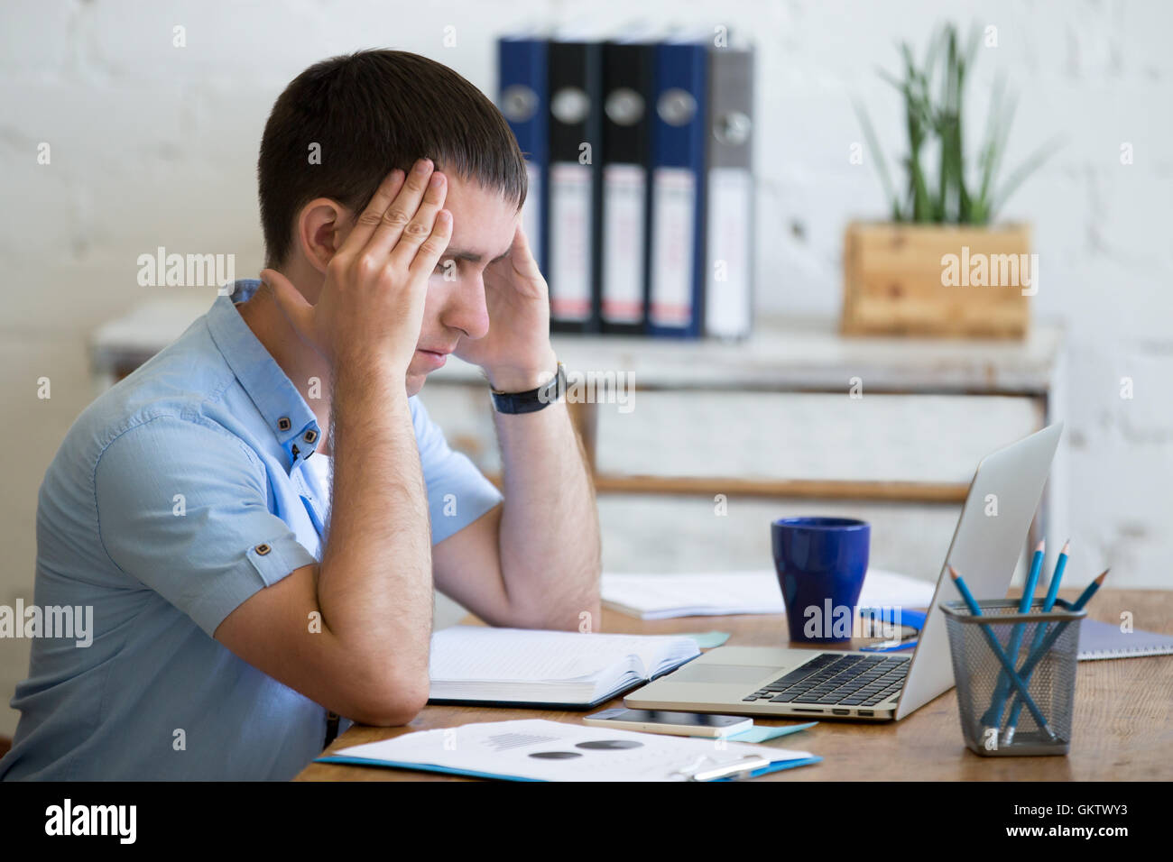 Young stressed businessman sitting in front of laptop and touching his head with pained expression. Business man feeling pain Stock Photo