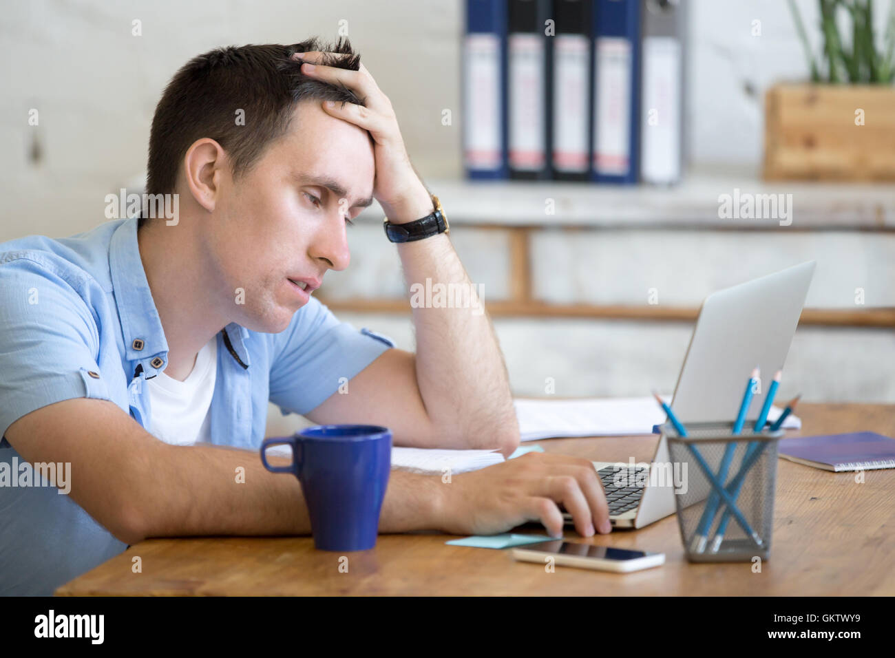 Portrait of young man sitting at the table in front of laptop, sleepy, tired, overworked or lazy to work. Attractive business Stock Photo