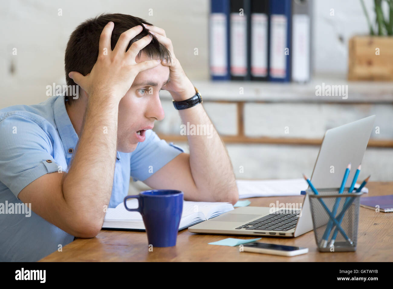 Young stressed businessman sitting with laptop and touching head with shocked facial expression. Surprised business man looking Stock Photo