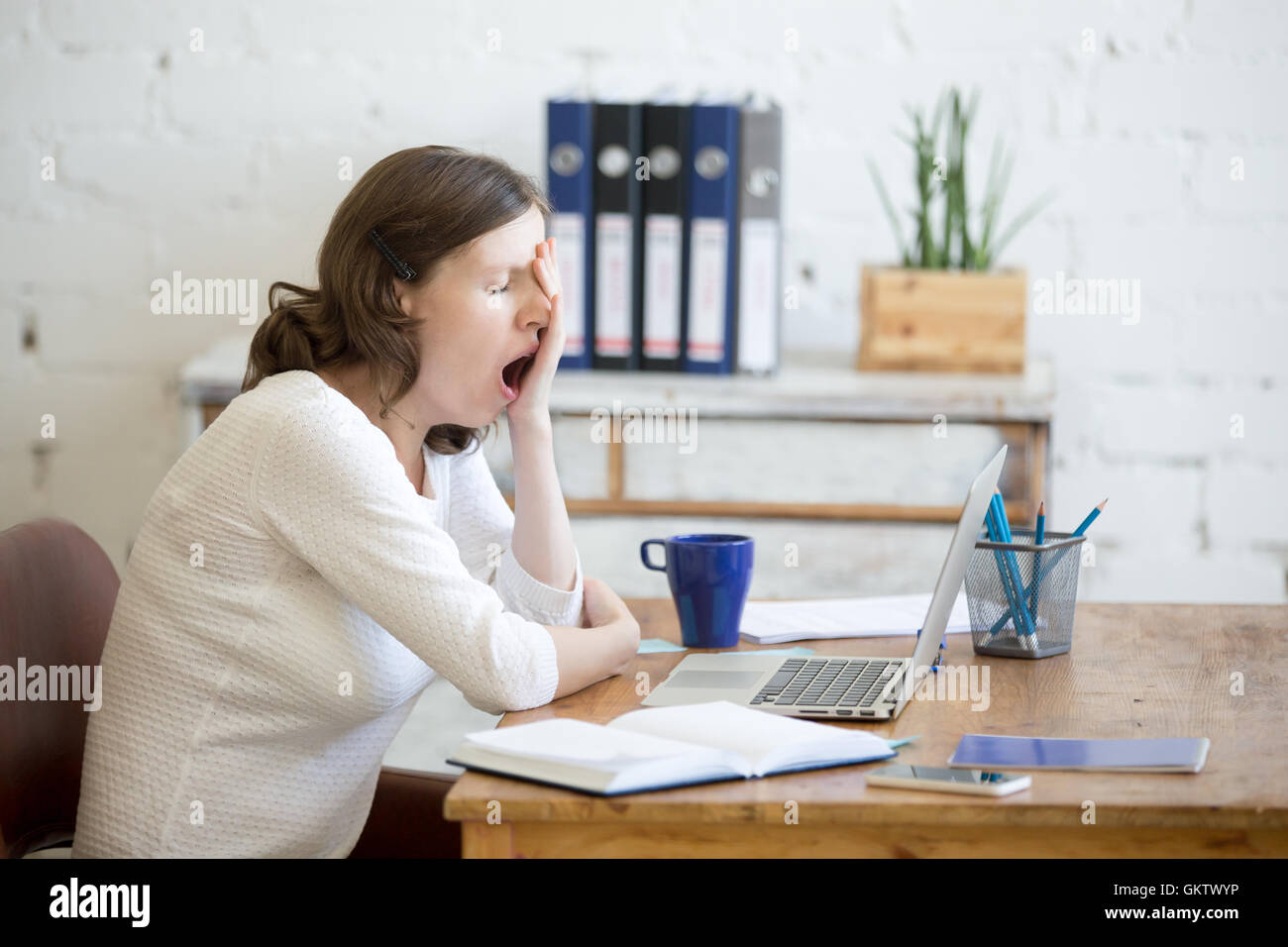 Portrait of young woman sitting at table in front of laptop, sleepy, tired, overworked, lazy to work. Attractive business woman Stock Photo