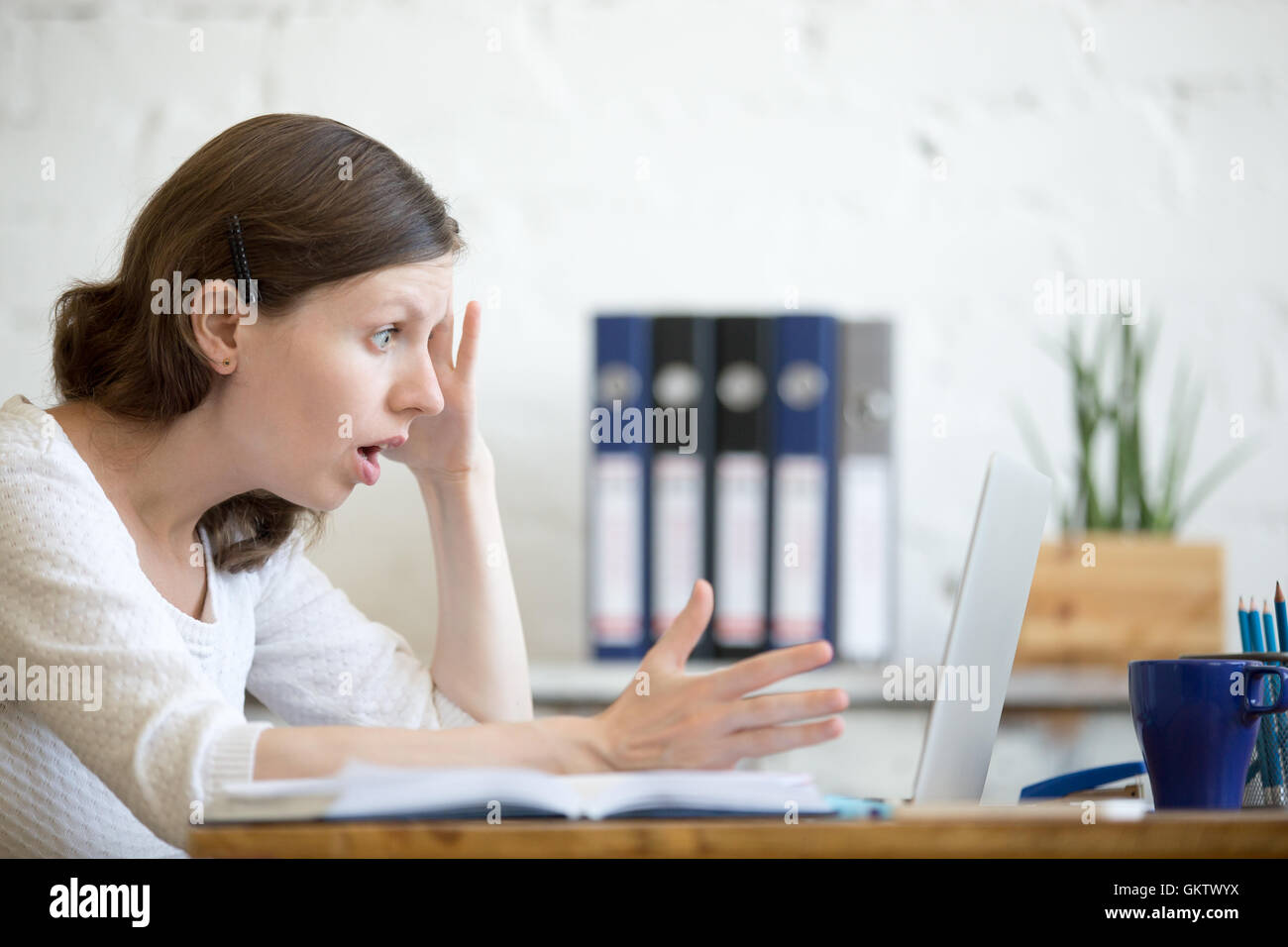 Young stressed businesswoman sitting with laptop and touching head with shocked facial expression. Surprised business person Stock Photo