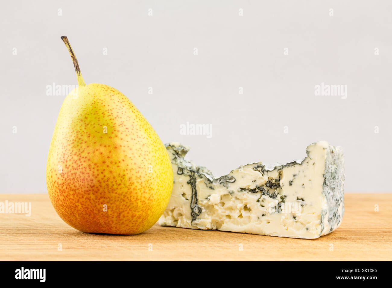 Close-up of a small  bell shaped forelle pears and Danish Rosenborg blue cheese wedge on wooden cutting board. Stock Photo