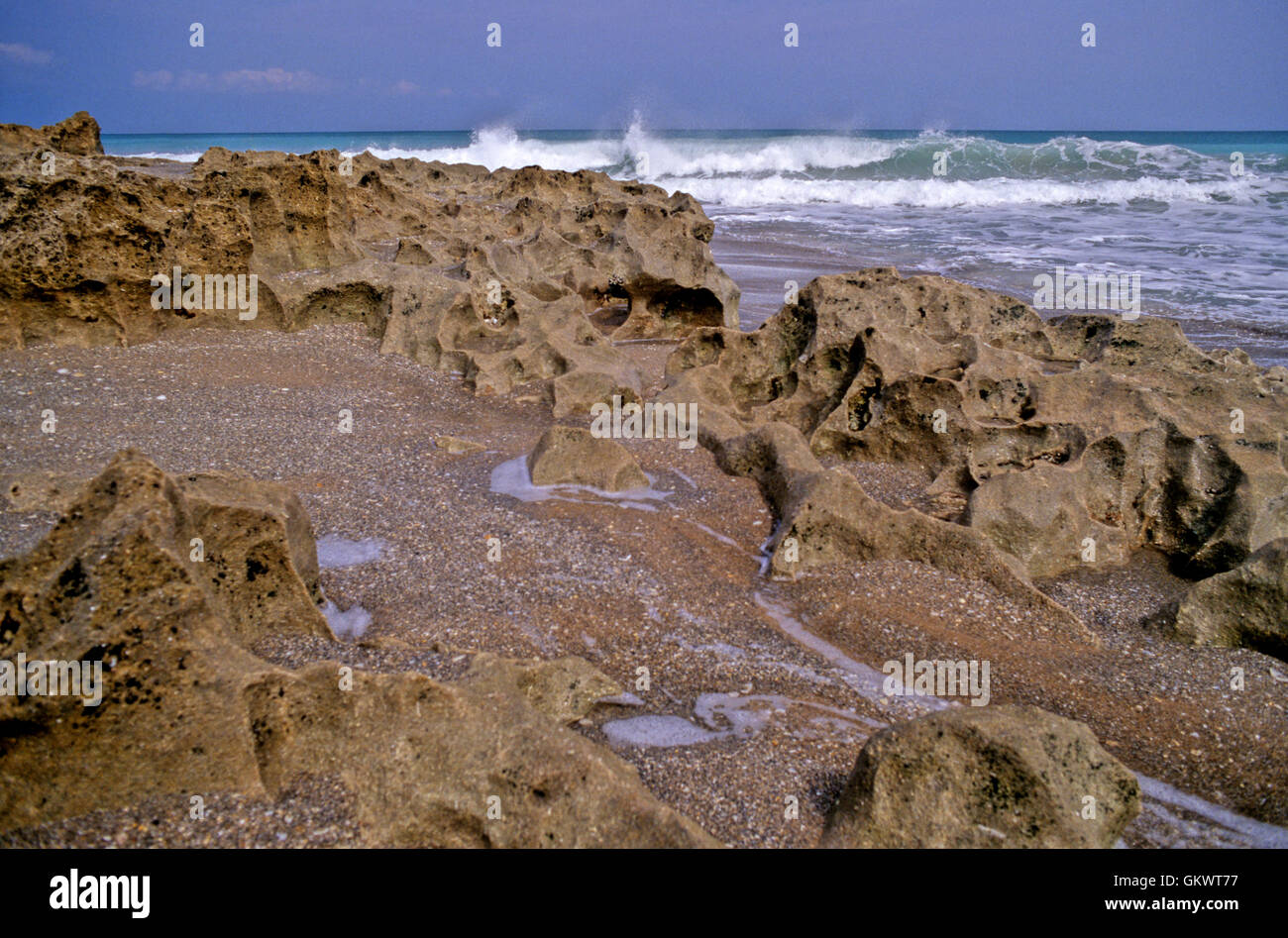 Blowing Rocks Beach in Jupiter, Florida features unique red rock formations complemented by shoreline breakers and blue surf. Stock Photo