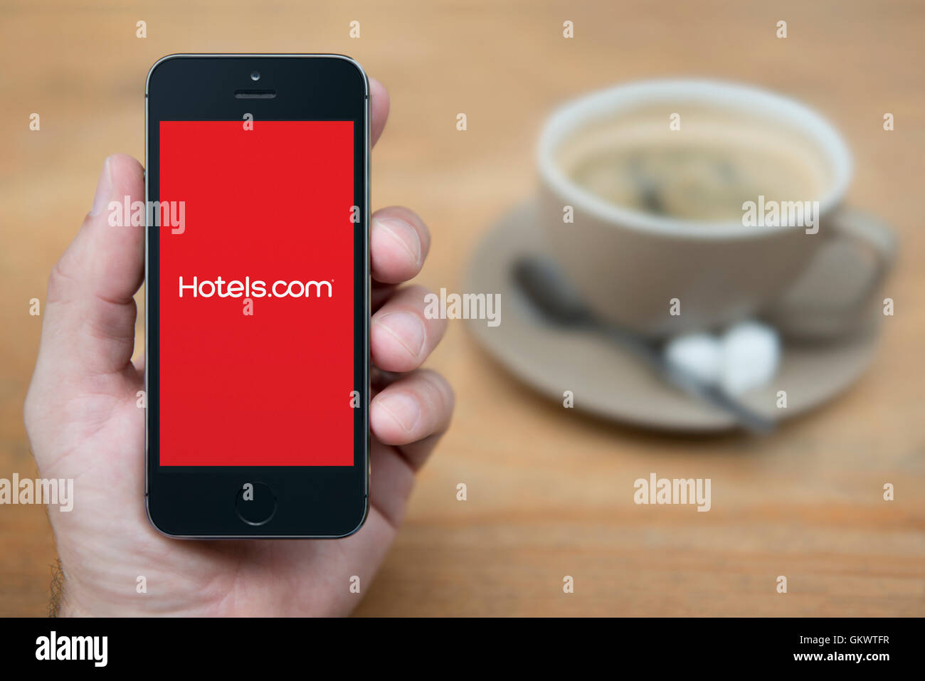 A man looks at his iPhone which displays the Hotels.com logo, while sat with a cup of coffee (Editorial use only). Stock Photo