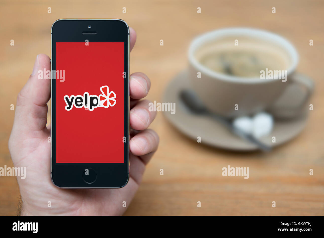 A man looks at his iPhone which displays the Yelp logo, while sat with a cup of coffee (Editorial use only). Stock Photo