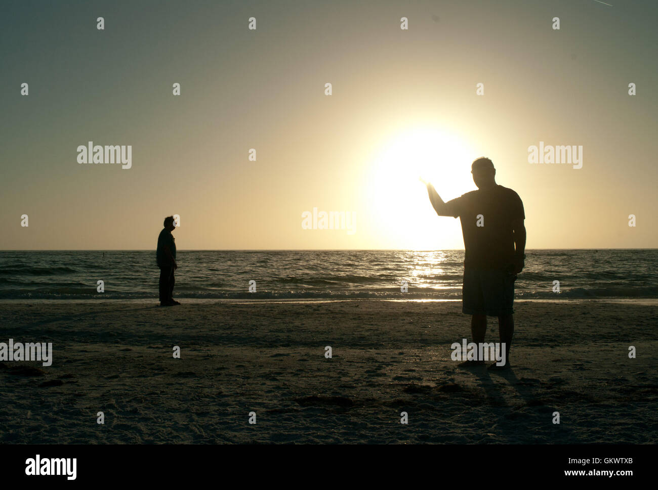 Two men stand at the seashore on the Gulf of Mexico, backlit by the setting sun. Stock Photo