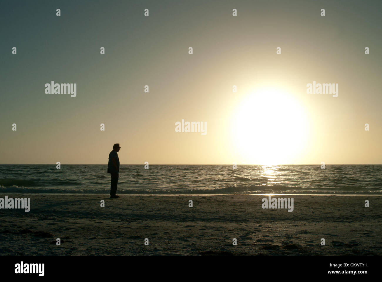A man stands at the seashore on the Gulf of Mexico backlit by the setting sun. Stock Photo