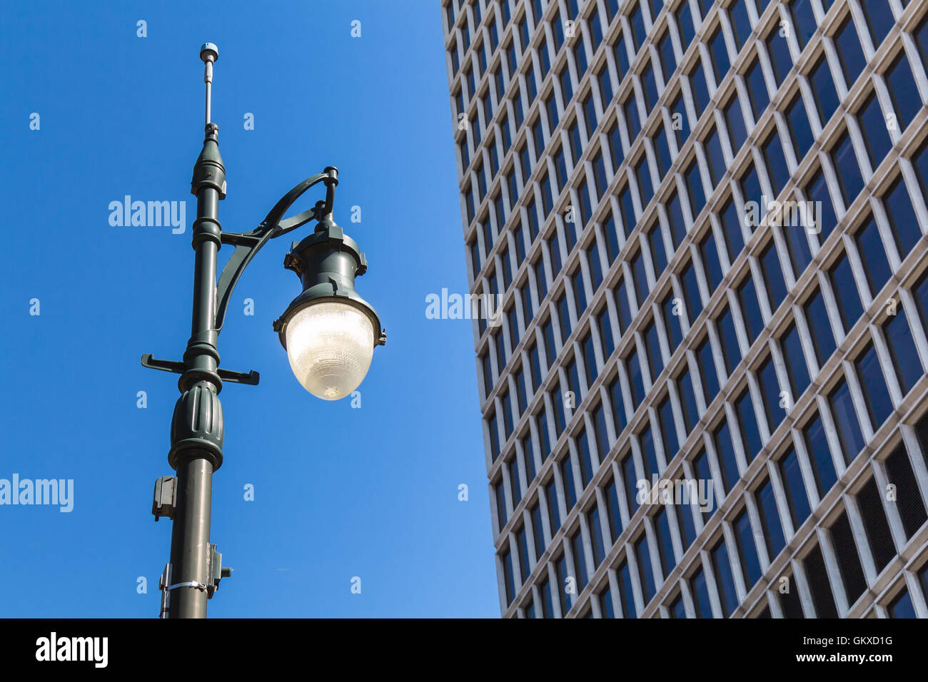 Old design of a street lamp, which is still on in spite of the blue sky day. Detail of a skyscraper. Downtown Detroit, Michigan, Stock Photo