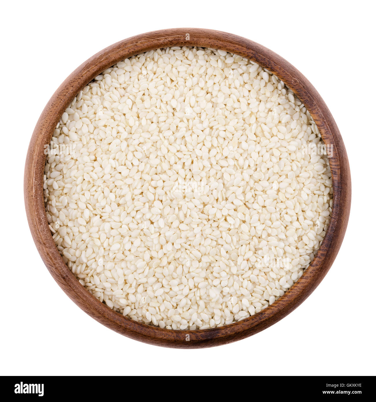 Sesame seeds in a wooden bowl on white background. Dried seeds with removed seed coats. Sesamum, also called benne. Stock Photo