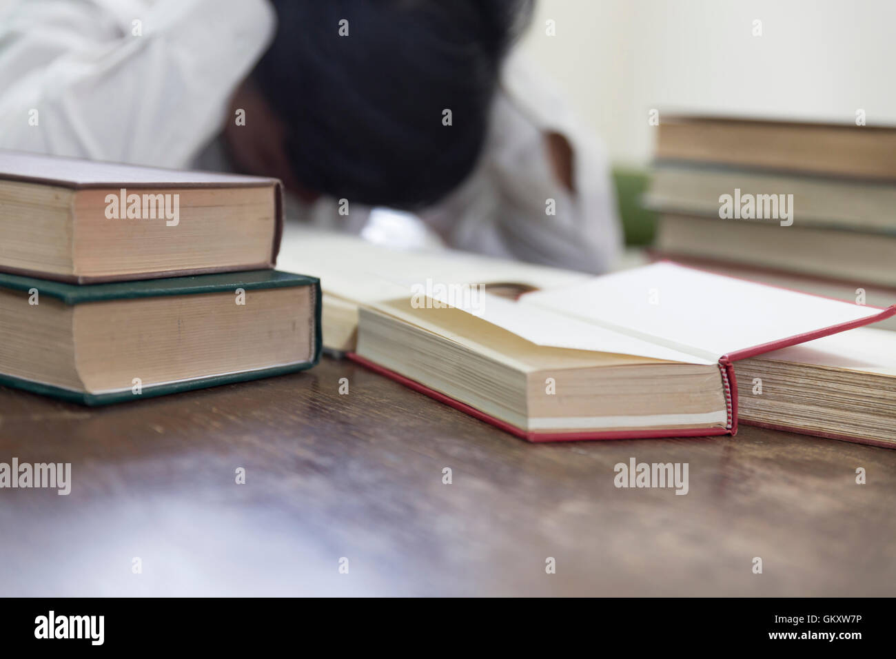 confused and upset man with textbook stack on wooden desk in library Stock Photo