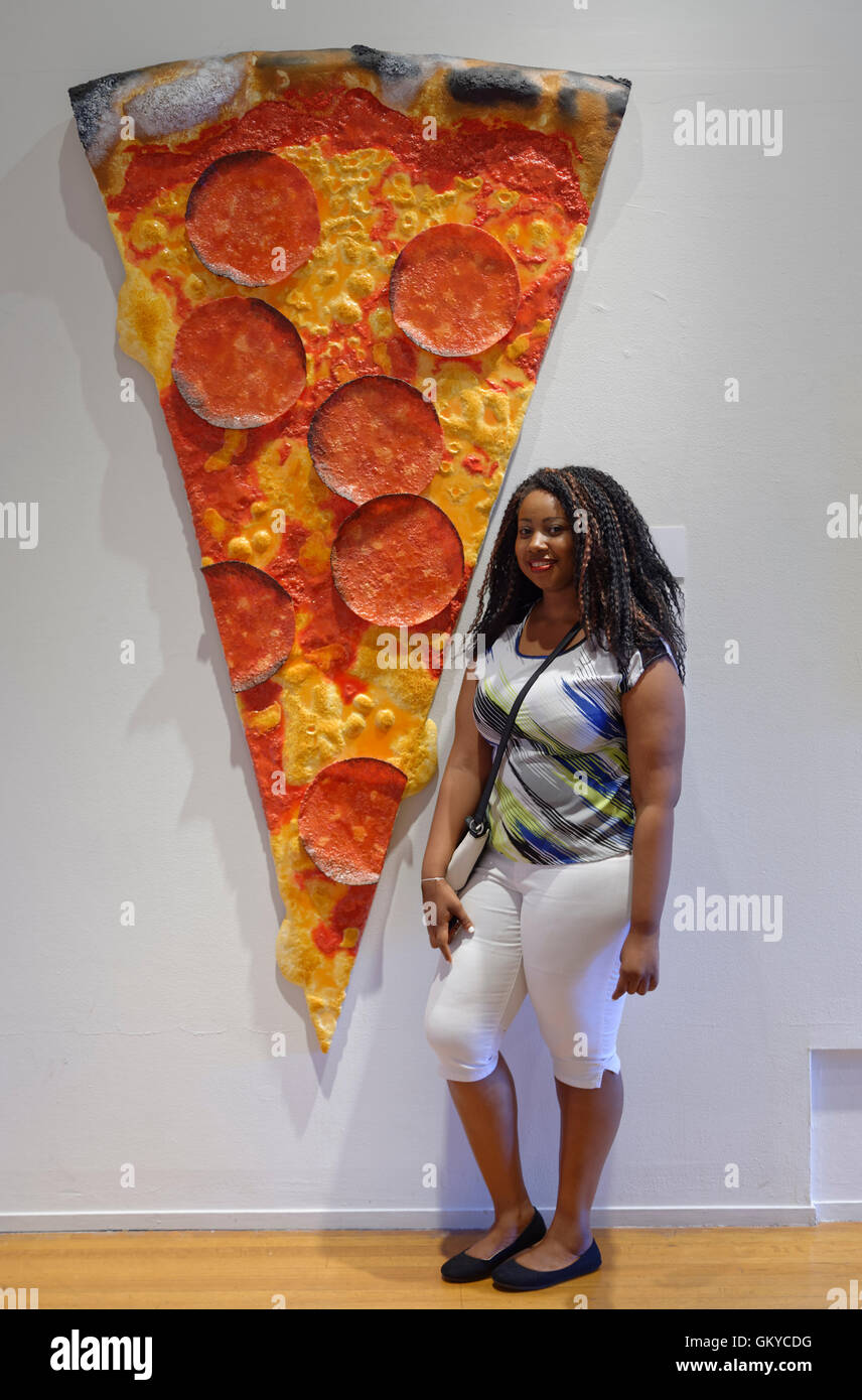 Roslyn Harbor, New York, USA. August 23, 2016. JESSICA, of Long Island, poses next to artwork 'Pizza' by artist Peter Anton (b. 1963, American) mixed media, of slice of Pizza with pepperoni slices, at Feast for the Eyes exhibition focusing on food and dining in art, at Nassau County Museum of Art in Long Island. Credit:  Ann E Parry/Alamy Live News Stock Photo