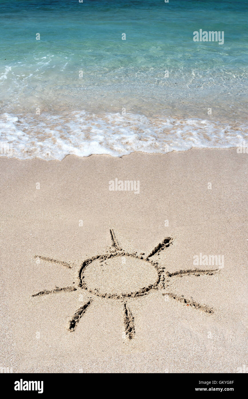 Hand drawn shining sun on beach sand at the edge of a calm blue sea and surf conceptual of the summer season and vacations Stock Photo
