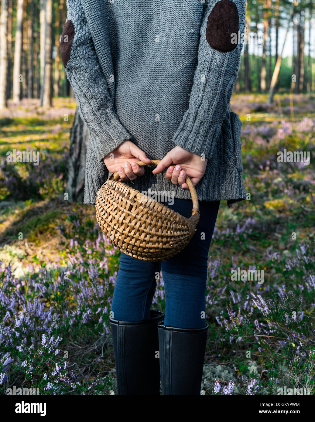 Girl standing back to camera in the forest and holding a basket. Stock Photo