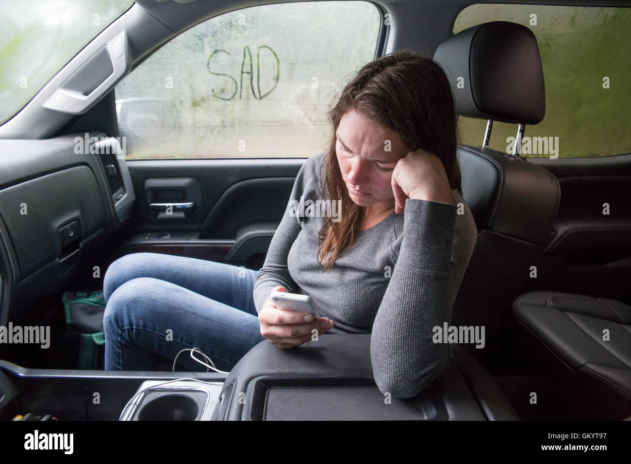 Woman is sad and uses phone to detach while sitting in truck. Stock Photo