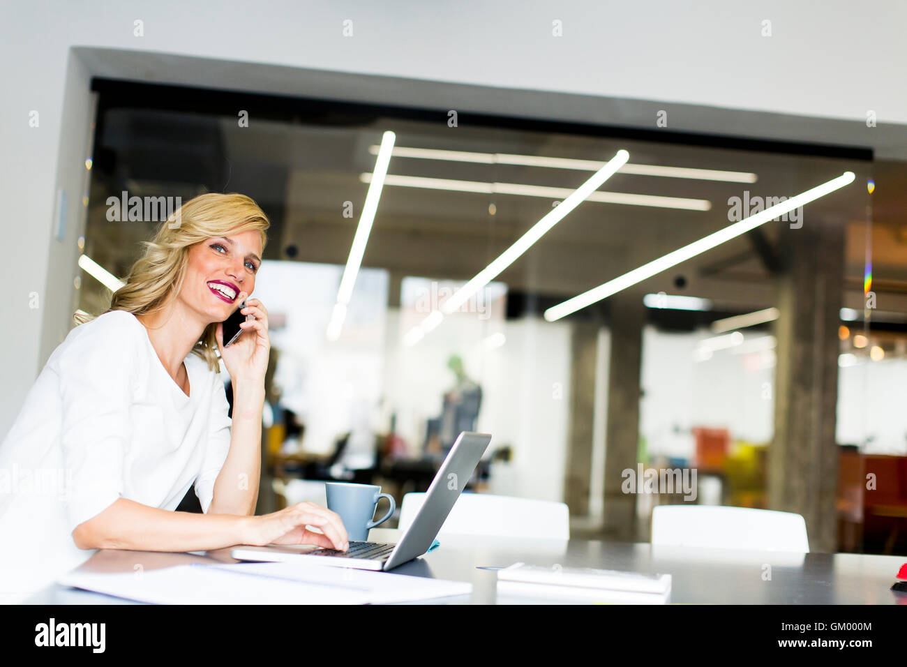 Young manageress working at her desk in the office taking a call on her mobile phone Stock Photo