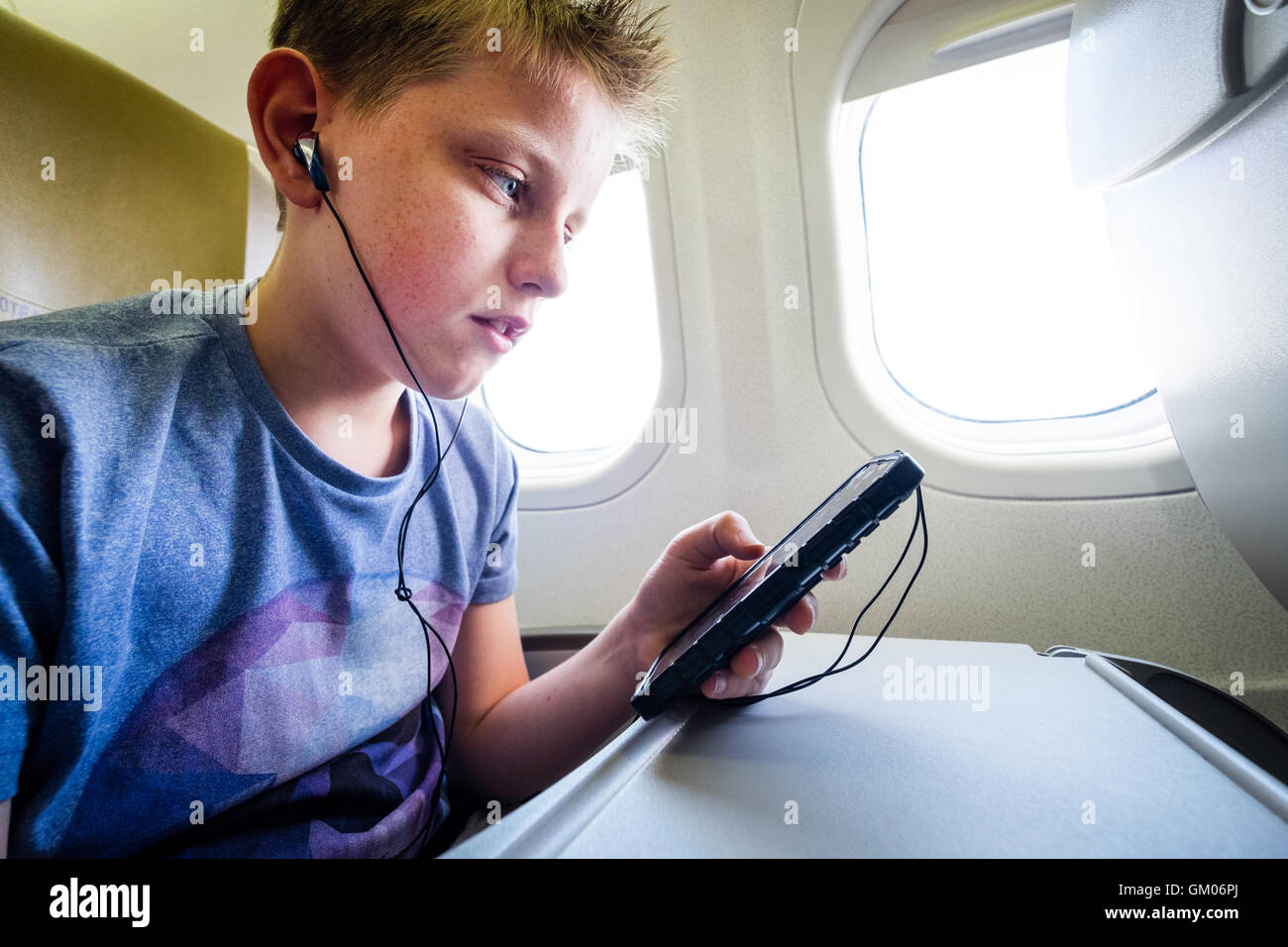 A teenage boy using his mobile phone during the flight on a plane to listen to music Stock Photo