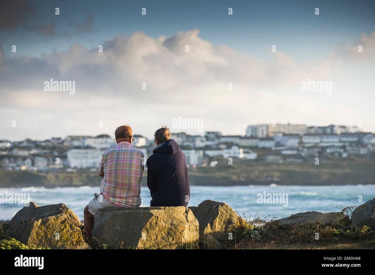 Two holidaymakers sit on rocks overlooking Fistral in Newquay, Cornwall. Stock Photo