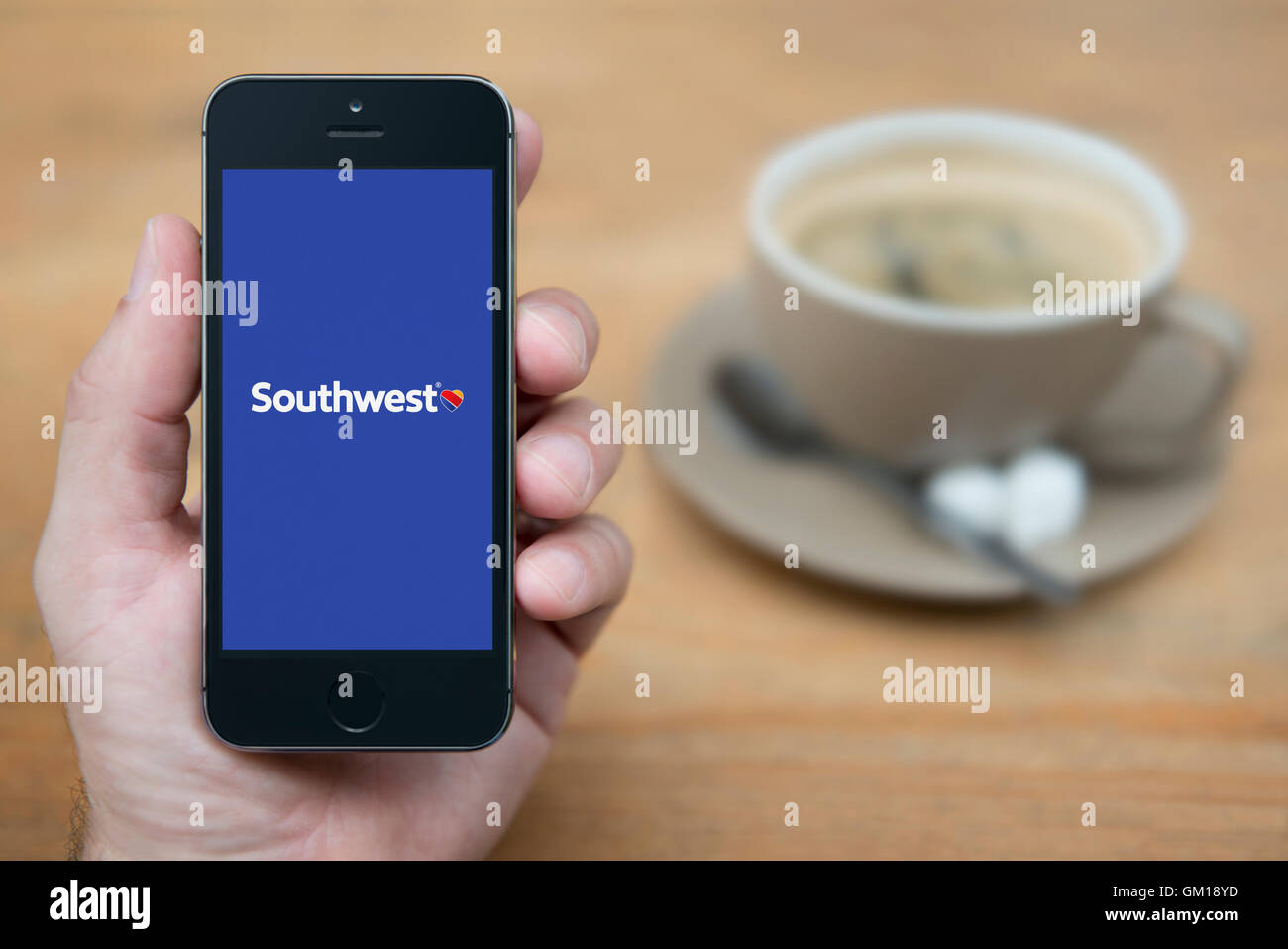 A man looks at his iPhone which displays the Southwest Airlines logo, while sat with a cup of coffee (Editorial use only). Stock Photo