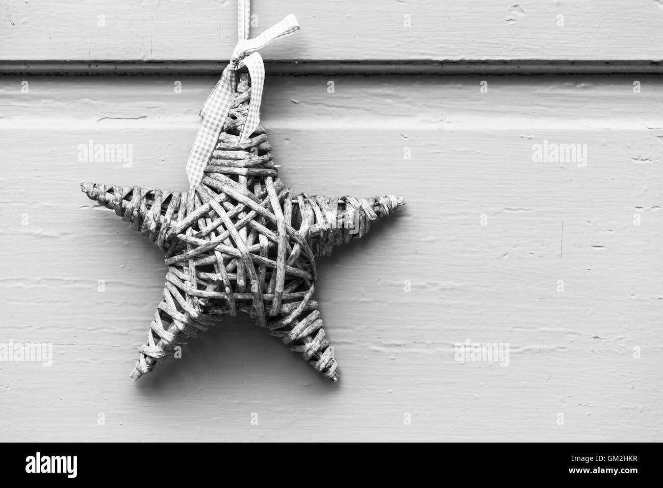 Wicker star hanging on white wooden wall, outdoor Christmas decoration. Black and white  background photo Stock Photo