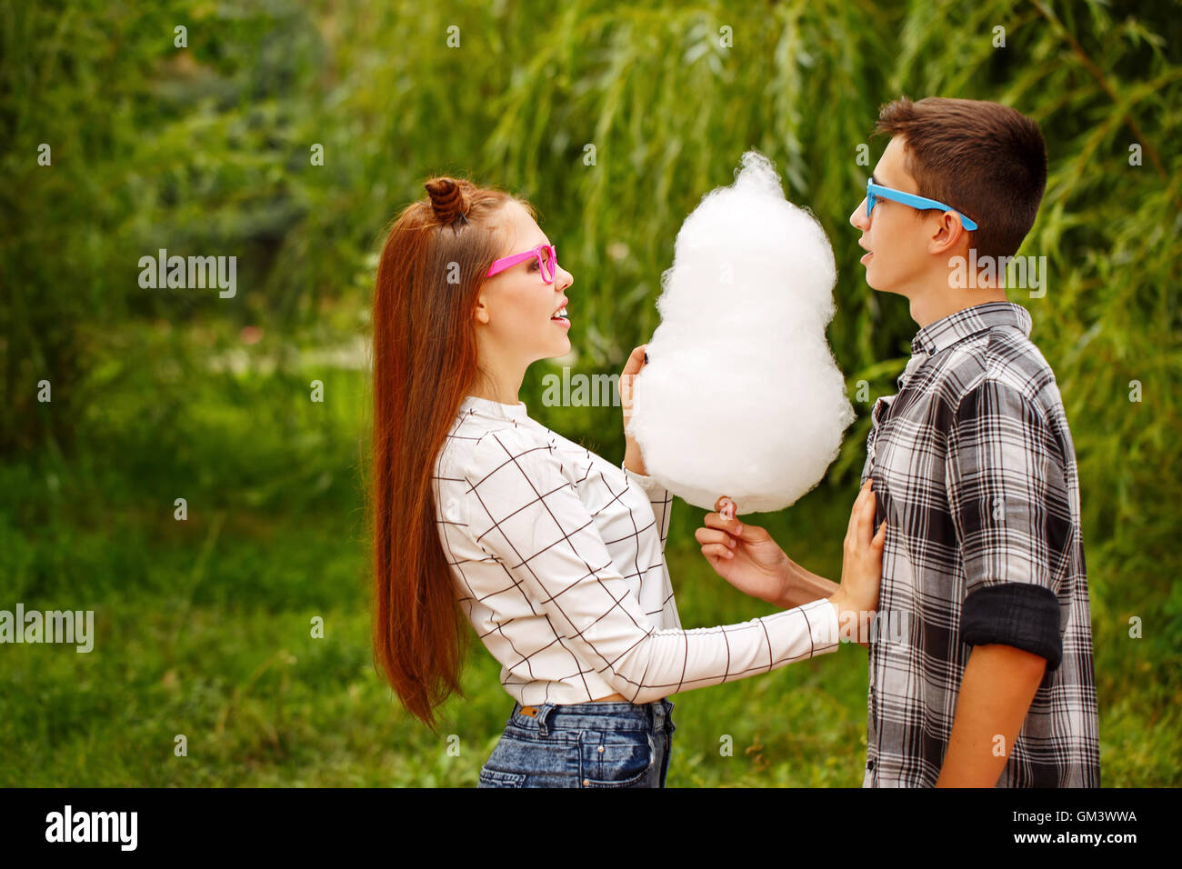 Loving couple teens eat cotton candy. Girlfriend and boyfriend together. They wear glasses. First love. He falls in love. Date. Stock Photo