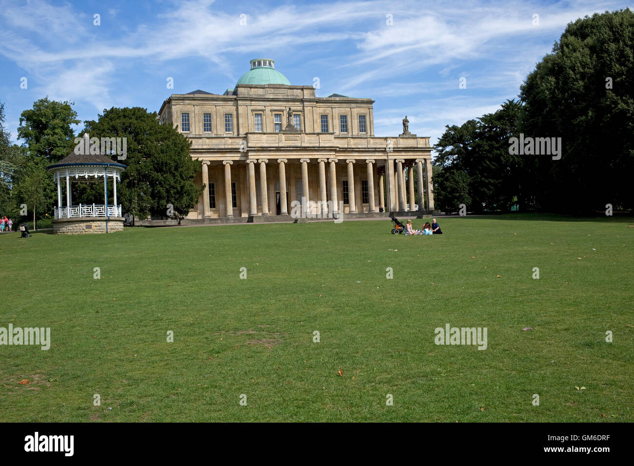 Family picnicing on lawn in front of Pittville pumproom the largest spa Grade 1 listed building historically dispensing health g Stock Photo