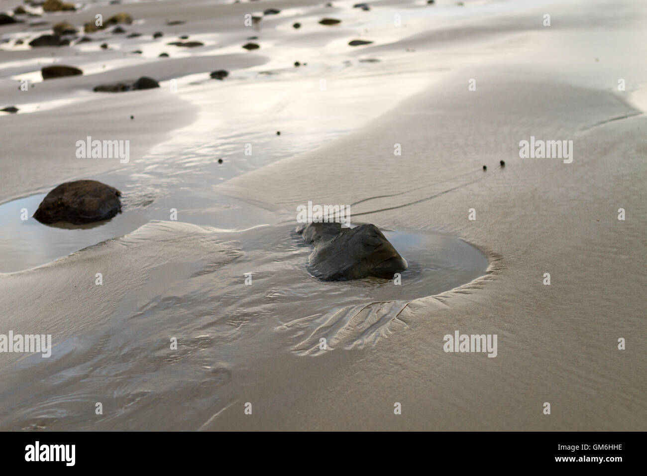 Ocean water pooling around rocks and wet sand at the beach Stock Photo