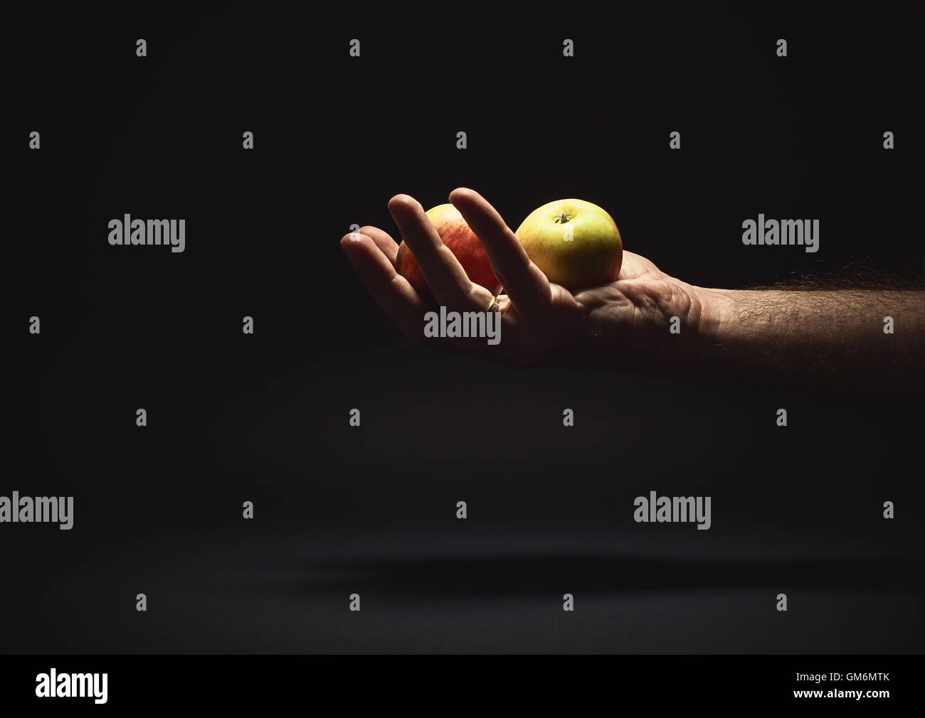 Conceptual composition, male hand holding two apples and giving it to someone. Stock Photo