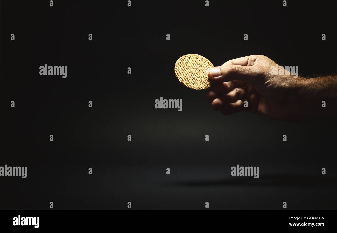 Conceptual composition, male hand holding a biscuit and giving it to someone. Stock Photo