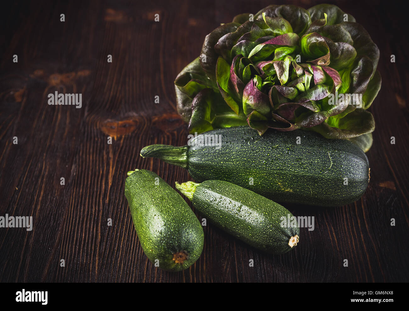Fresh zucchini with red oakleaf lettuce on wooden table Stock Photo